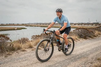 Cycliste sur un chemin côtier longeant les étangs de la Pointe du Salaison avec des flamants roses en arrière-plan